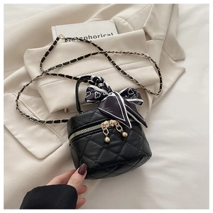 Detail of black quilted mini bucket bag with gold chain strap and decorative silk scarf