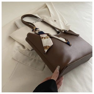 Detail of dark brown leather tote bag with silk scarf on handle and contrast stitching