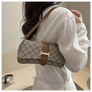 Detail view of printed canvas baguette bag with brown leather strap and gold H-clasp