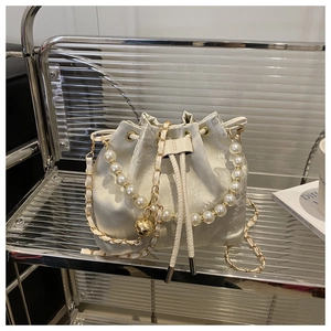 Detail of champagne satin bucket bag with pearl handle and golden jacquard texture