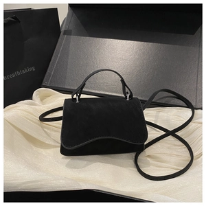 Detail of black crossbody bag with wavy flap edge on white silk and gift packaging
