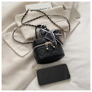 Mini black quilted chain bag with silk scarf handle detail next to a smartphone