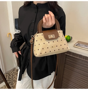 Detailed view of polka dot crossbody bag with golden twist lock and brown leather handle