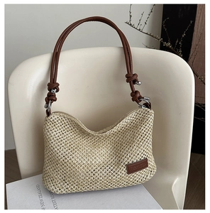 Close-up of woven straw bag with brown faux leather strap and brand logo detail
