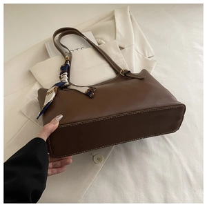 Detail of a brown leather tote bag featuring contrast stitching and a silk scarf handle