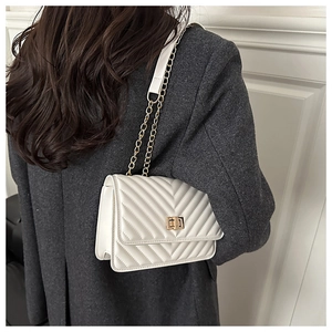 Close-up of white quilted chain bag with gold turn-lock on a grey tweed blazer