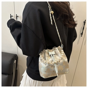Detail of blue satin bucket bag with gold embroidery and pearl handle worn by a model