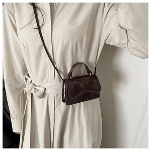 Detail of a dark brown patent leather mini square bag with glossy finish on a cream dress