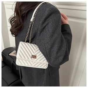 Detail of white V-quilted small square bag with gold twist lock and chain strap on shoulder