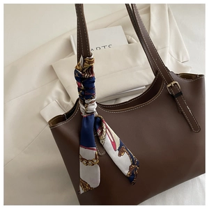 Close-up of brown leather tote bag detail with white stitching and floral silk scarf accessory