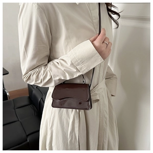 Detail of dark brown patent leather mini crossbody bag worn by a model in casual style