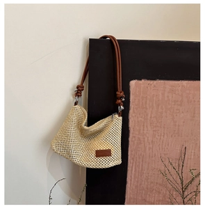 Detailed macro view of woven straw shoulder bag featuring brown leather strap and logo patch