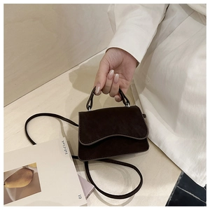 Detail of dark brown suede mini bag with a unique wavy flap and top handle held by hand
