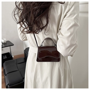 Detail of a dark brown patent leather mini bag with a top handle and slim strap