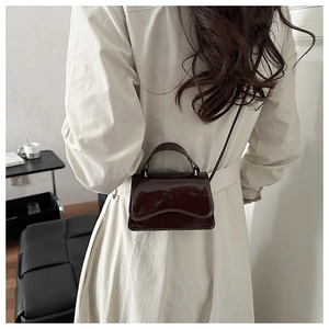 Detail of dark brown patent leather mini bag with wave-edge flap and mirror shine