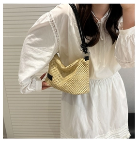 Detail of light beige woven straw bag featuring black leather strap and metal ring knots
