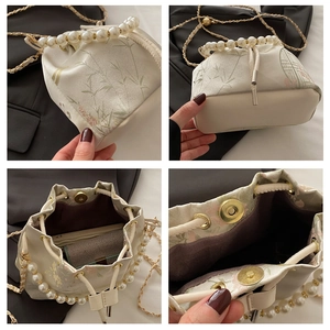 Detail view of pearl handle, floral embroidery, and gold chain on the satin bucket bag