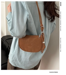 Detail of a brown leather crescent shoulder bag featuring knot-tied straps and logo texture