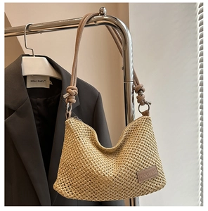 Detail of woven straw tote bag featuring leather shoulder strap and logo patch