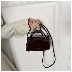 Detail of burgundy patent leather mini bag with curved base and silver hardware accents