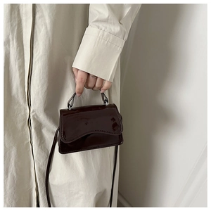 Detail of a dark brown patent leather mini bag with a glossy finish and top handle