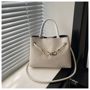 Detailed view of beige woven tote bag with gold knot hardware and textured finish