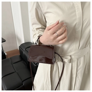 Detail of dark brown patent leather mini bag with glossy finish and metal buckle
