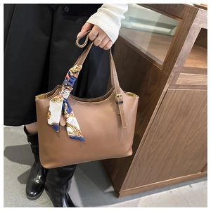 Close-up of caramel leather tote bag handle decorated with a blue patterned floral silk scarf