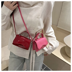 Close-up of vibrant red and pink glossy patent leather mini crossbody bags on a model
