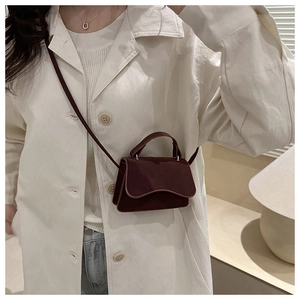 Detail of burgundy matte leather mini bag with unique wavy edge flap and top handle