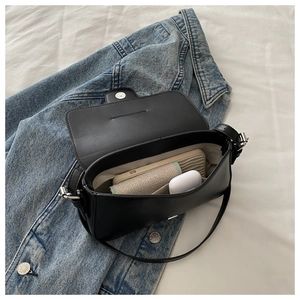 Black leather flap shoulder bag shown open with phone and earbuds on denim background
