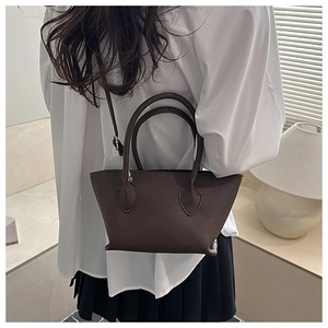 Detail of dark brown lychee leather tote bag with top handles shown in a warm lifestyle setting