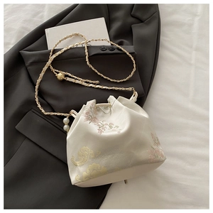 Detail of cream embroidery bucket bag with traditional floral patterns and pearl chain