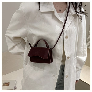 Detail of burgundy crossbody bag with wavy edge design held by model in white coat
