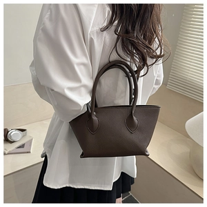Detail of a dark brown litchi pattern leather bucket bag held by a model in casual attire