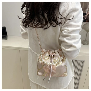 Detail of pink satin bucket bag featuring floral embroidery and pearl handle strap