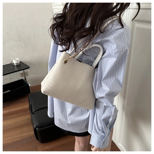 Detail of white woven leather handbag with dual handles and gold chain accents