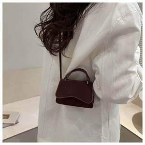 Detail of burgundy leather mini bag with wavy flap shown on a white shirt