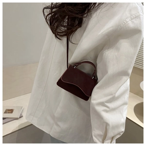 Detail shot of a burgundy faux leather crossbody bag worn over a white oversized shirt