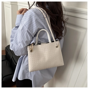 Detail of white woven leather handbag with circular handle and gold hardware on shoulder