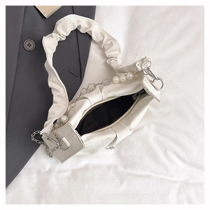 Detail of white pleated cloud handbag featuring decorative pearl and floral chain strap