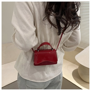 Red patent leather mini handbag with wavy flap worn by model in a warm interior setting