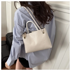 Detailed close-up of beige woven texture handbag with golden metal hardware and strap