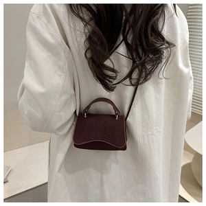 Detail of burgundy leather mini bag with wave flap design and delicate shoulder strap