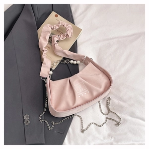 Detailed view of pink pleated handbag with pearl chain decoration on fabric background
