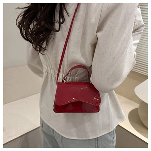 Close-up of a red patent leather crossbody bag with a glossy finish and flap design