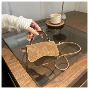 Detail of a brown leather crossbody bag with a wave flap design in a cafe setting