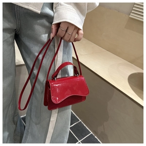 Close-up of a glossy red patent leather mini handbag with wavy flap held by a model