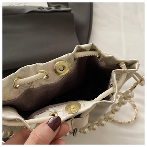 Detailed close-up of floral drawstring bucket bag with pearl chain and magnetic closure