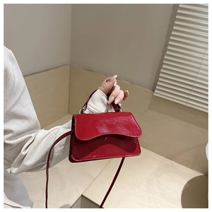 Detail of a shiny red patent leather mini handbag with top handle and crossbody strap